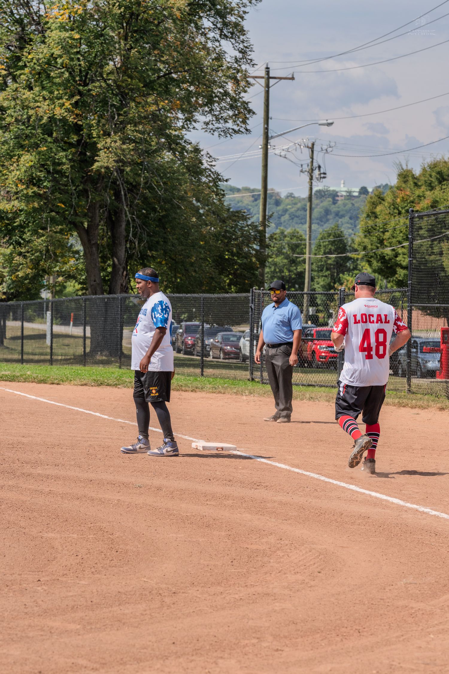 Softball players and umpire on field during a recreational league game on a sunny day.