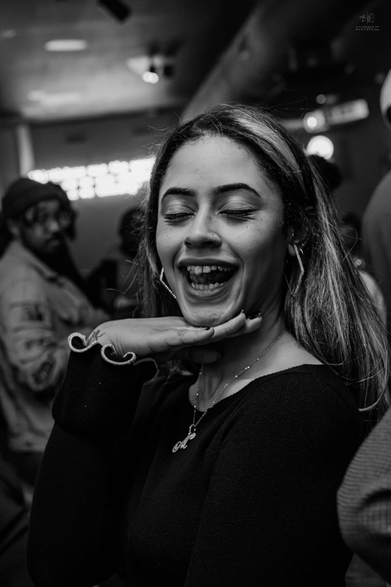 Black and white photo of a laughing woman in a black top, blowing a kiss at a social gathering.