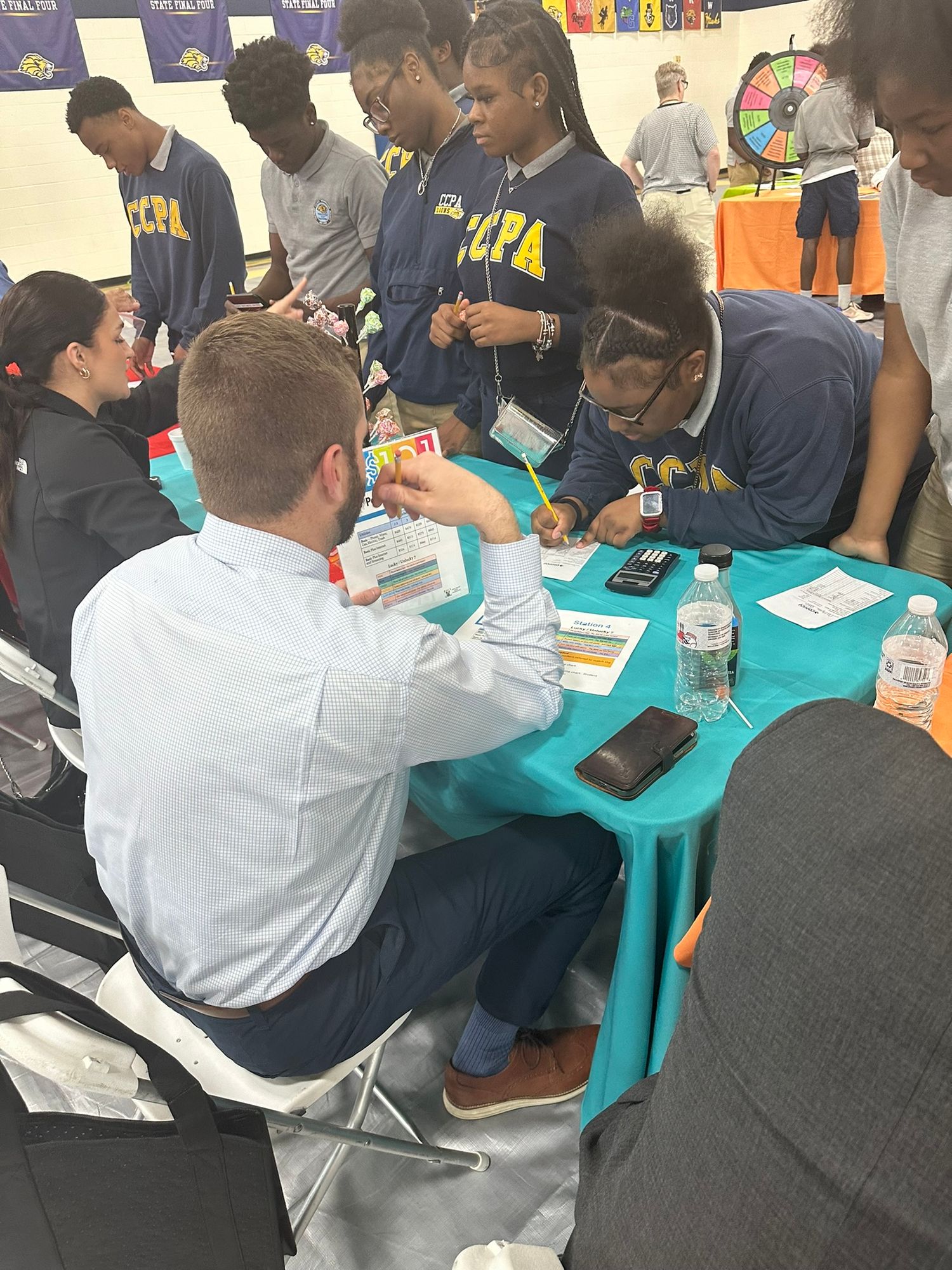 Students in HCPA uniforms engage with a professional at a teal table during an educational career fair event.