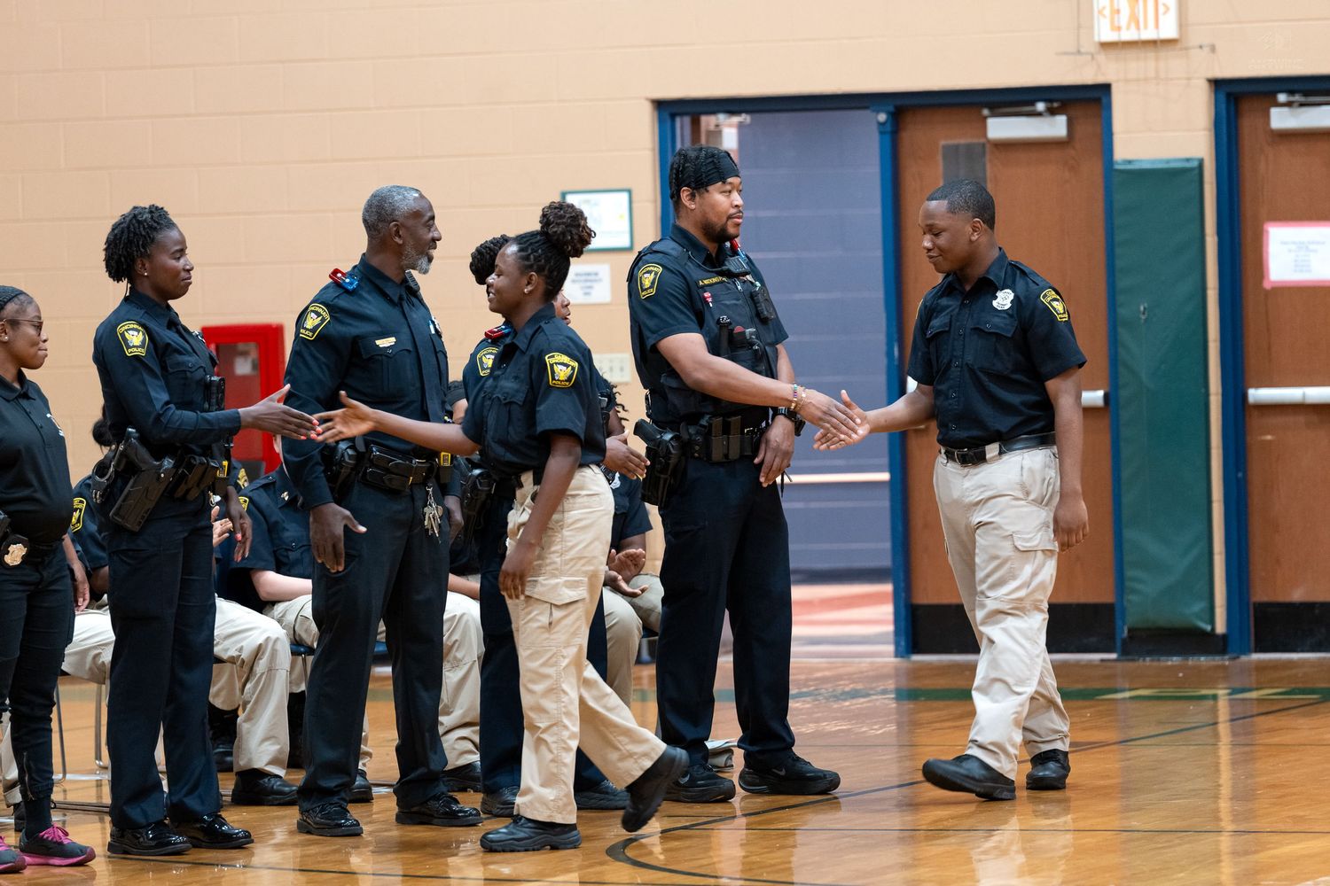 Law enforcement officers in uniform shaking hands during an indoor ceremony in a school gymnasium.