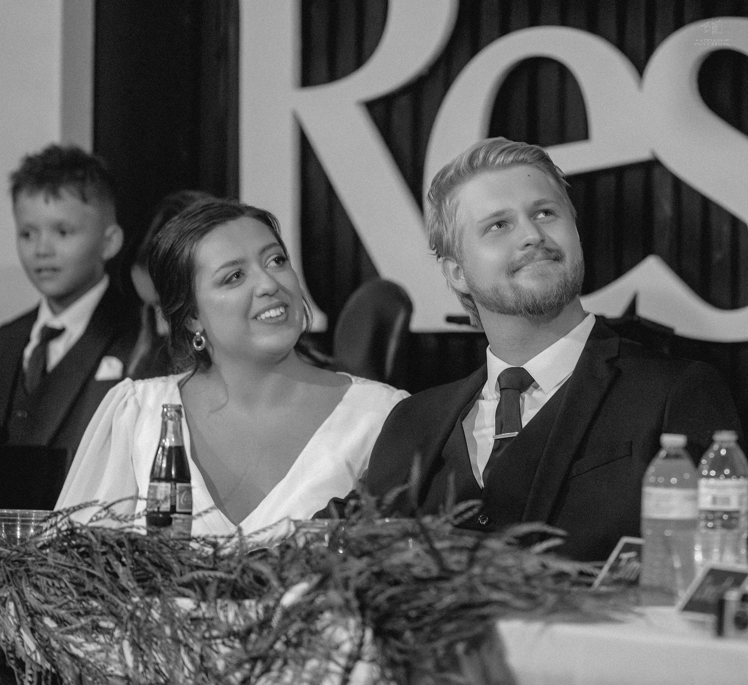 Bride and groom smile warmly while seated at the head table during their wedding reception.