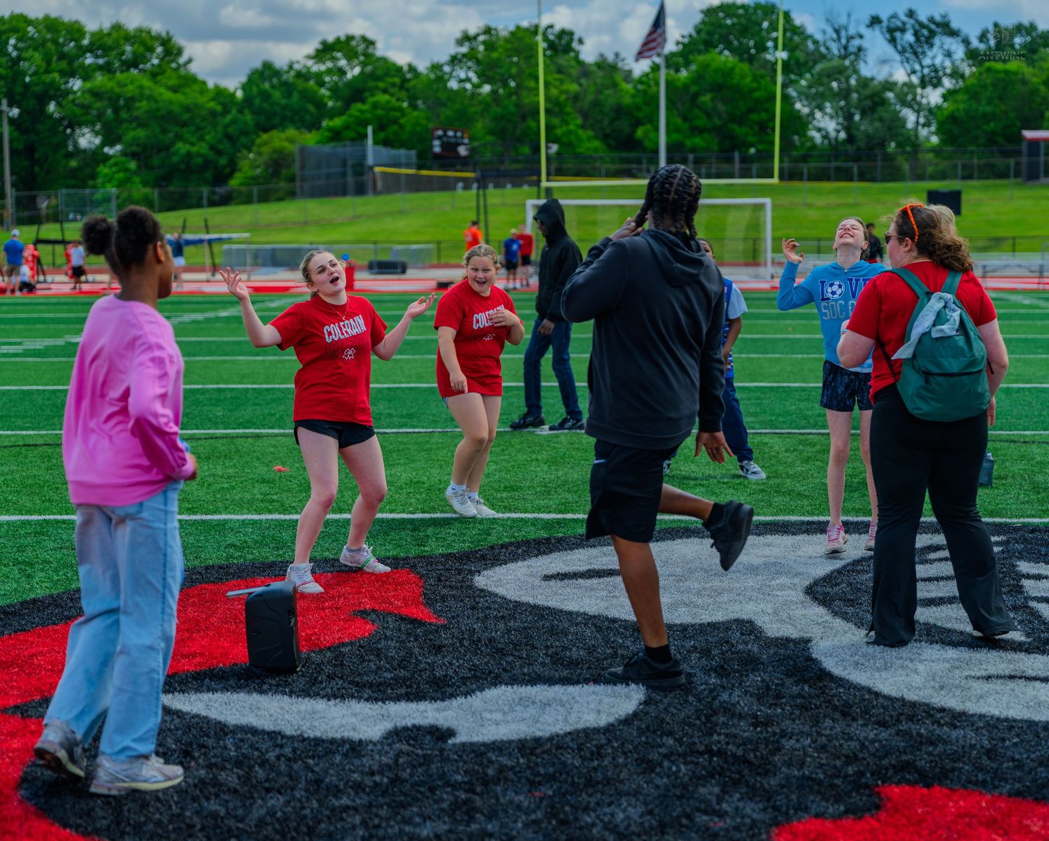 Students playing outdoor games on a red and black turf football field during a school event.