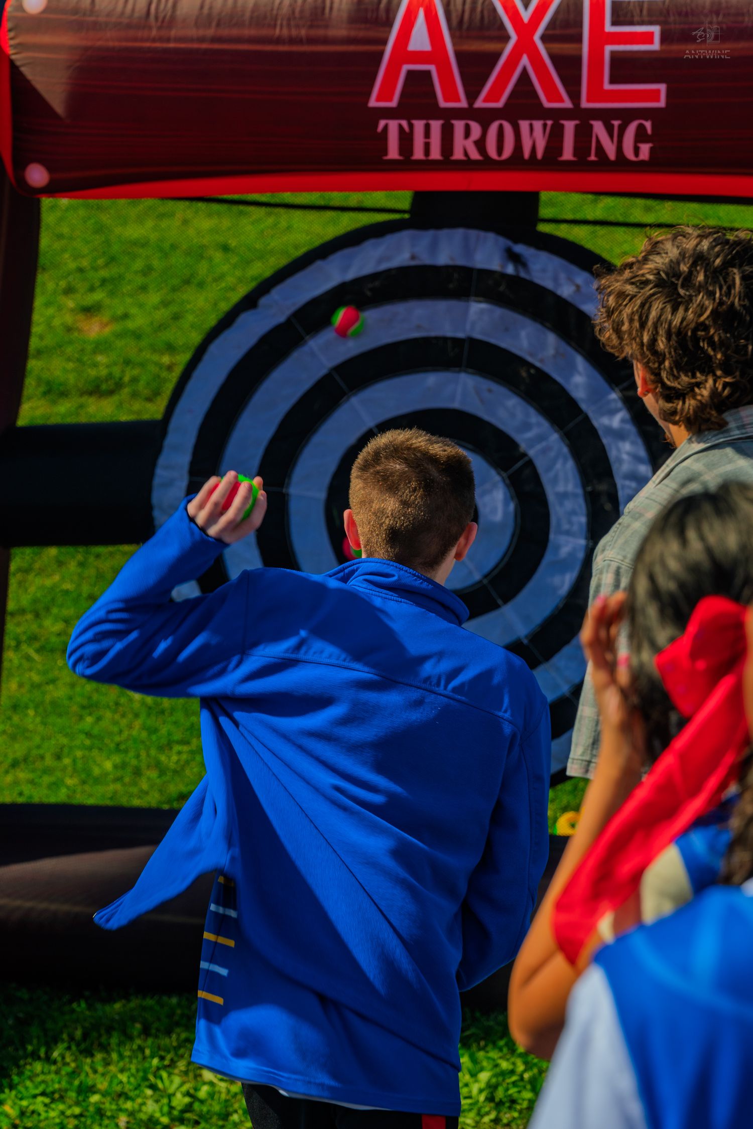 Person in blue jacket throwing axe at bullseye target at outdoor axe throwing activity.