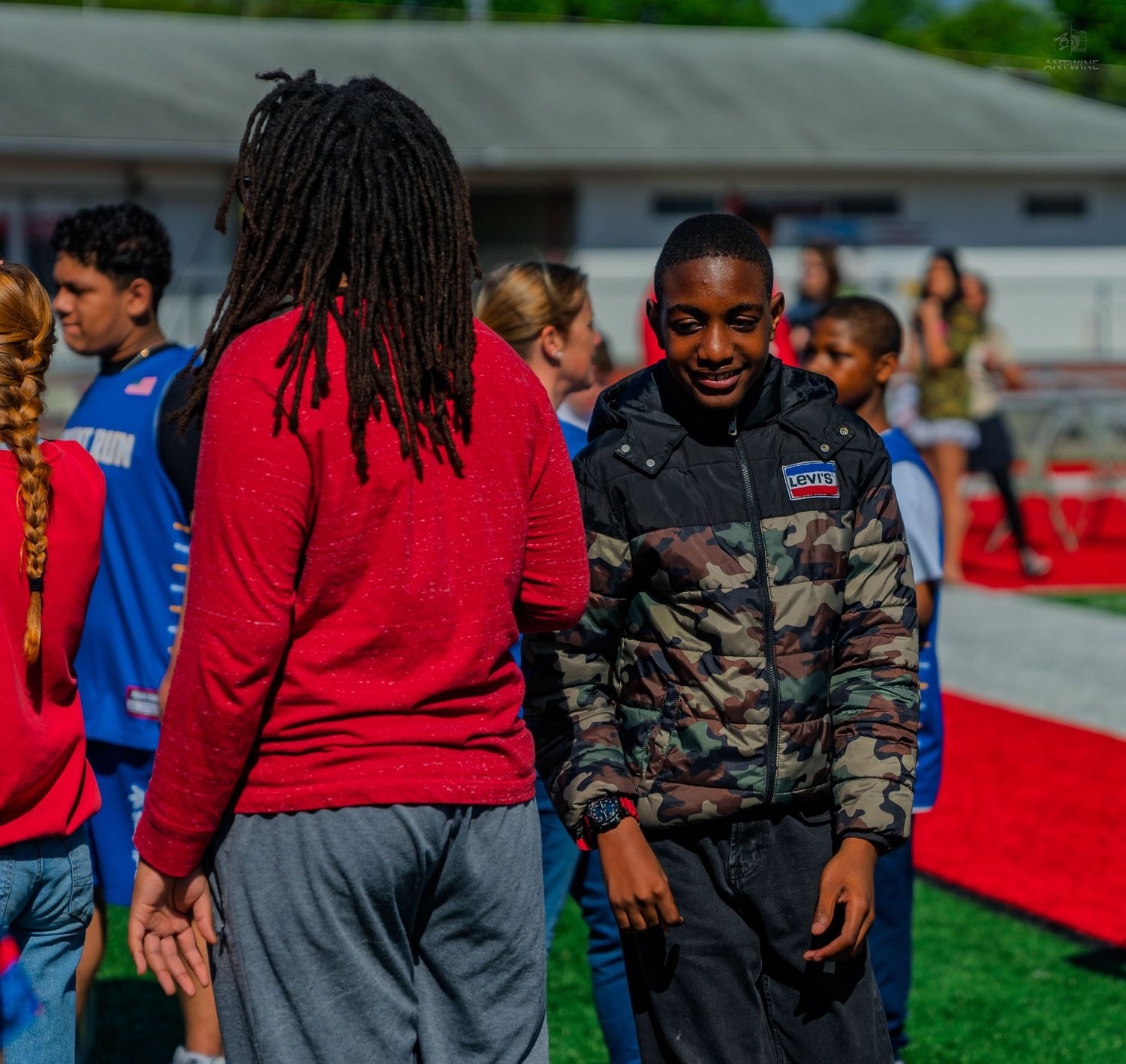 Two young athletes in sportswear interact on a red track during an outdoor school sports event.