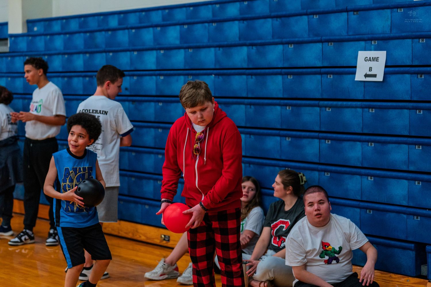 Students playing basketball in a school gymnasium with blue bleachers during a youth sports event.