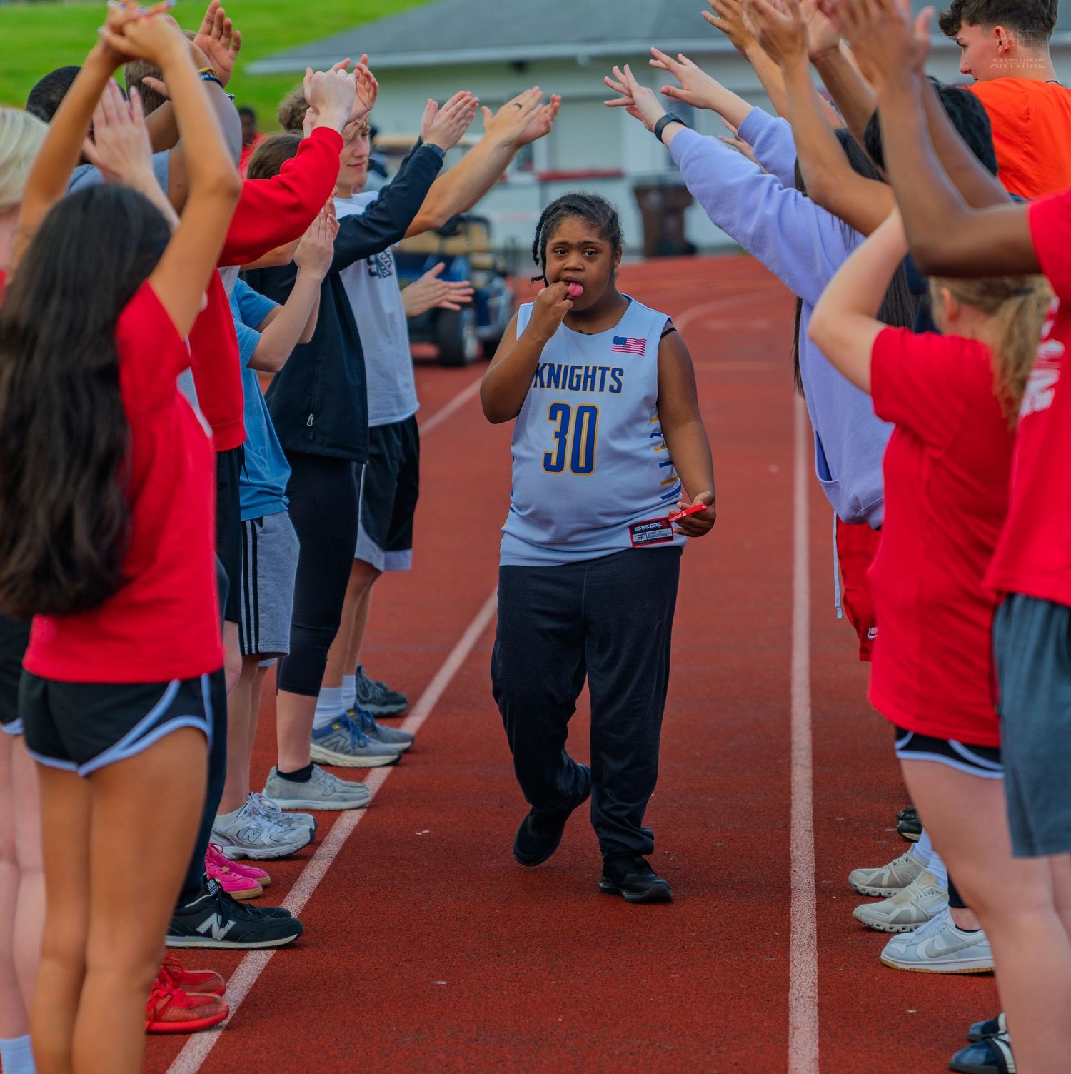 Athlete in Knights #30 jersey walks triumphantly through a tunnel of raised hands on a track.