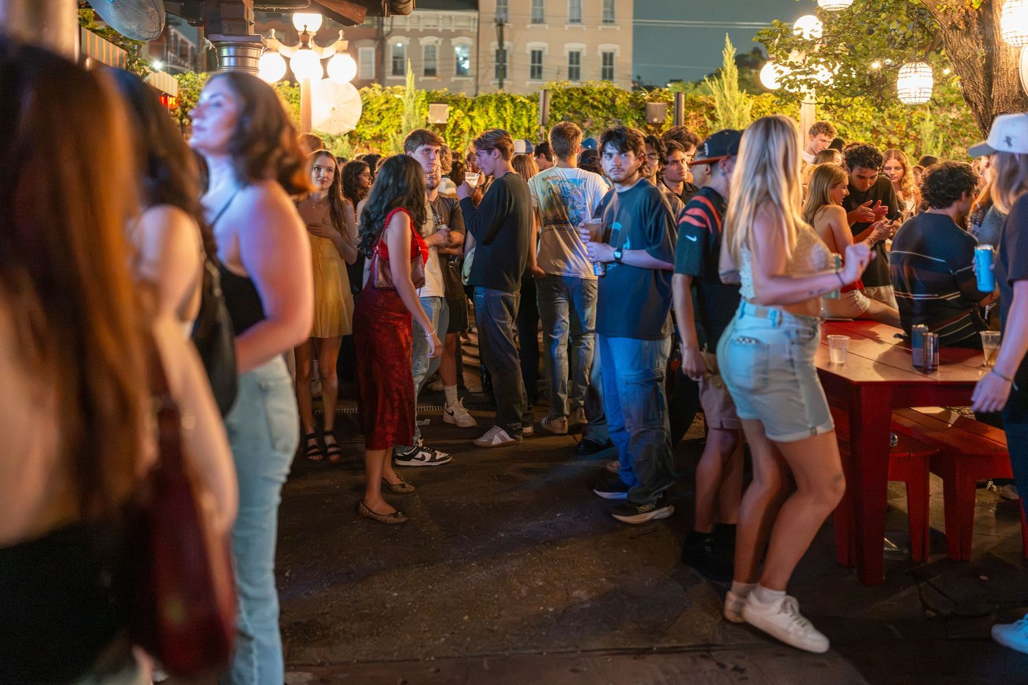 Crowd of young people socializing at an outdoor night market street party with warm string lights.
