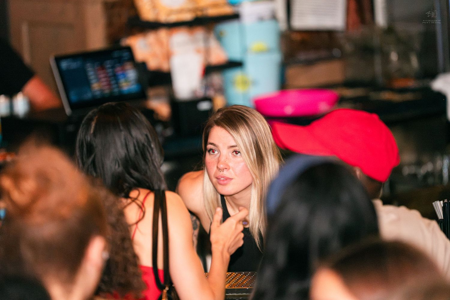 Blonde woman in black top engages in conversation at a busy bar or club.