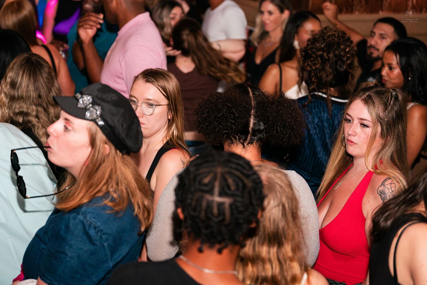 Young women in casual attire mingling in a crowded nightclub, woman in red dress nearby.