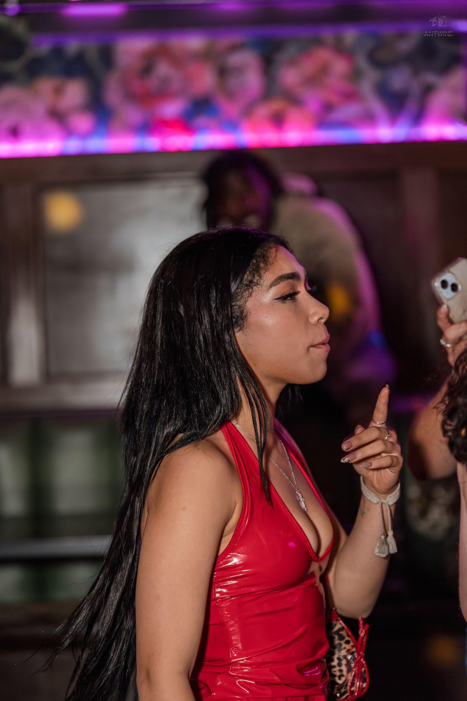 Young woman in red leather dress holds up finger while socializing at a vibrant nightclub event.