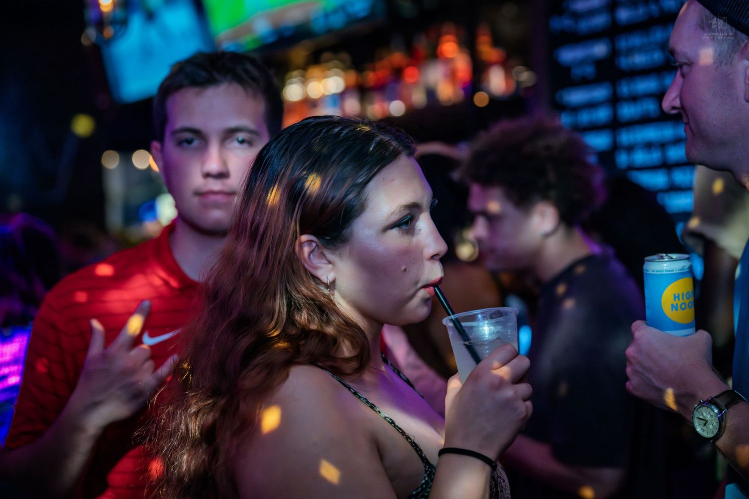 Young woman sipping a drink at a lively nightclub bar.
