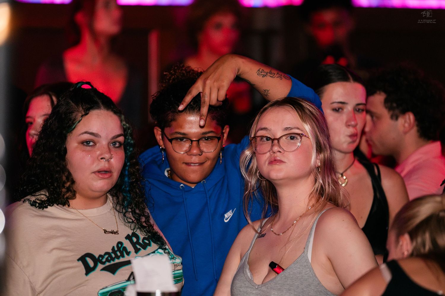 Three young people at a nightclub, posing together under red neon lights in a lively crowd.