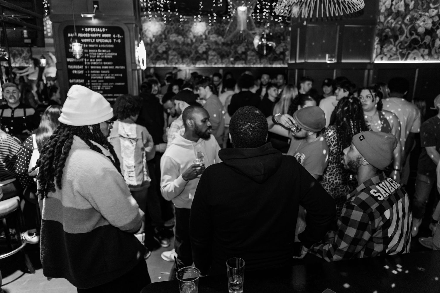Black and white photo of a lively crowded nightclub party with people socializing and dancing indoors.