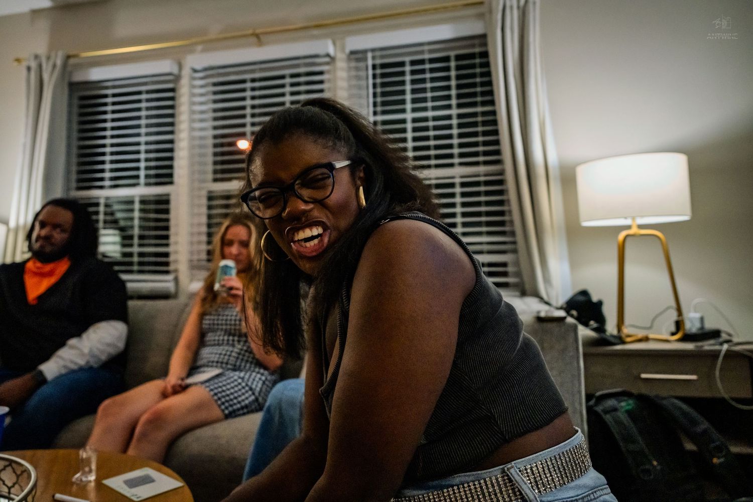 Young woman with glasses laughing joyfully while sitting on a couch at a house party.