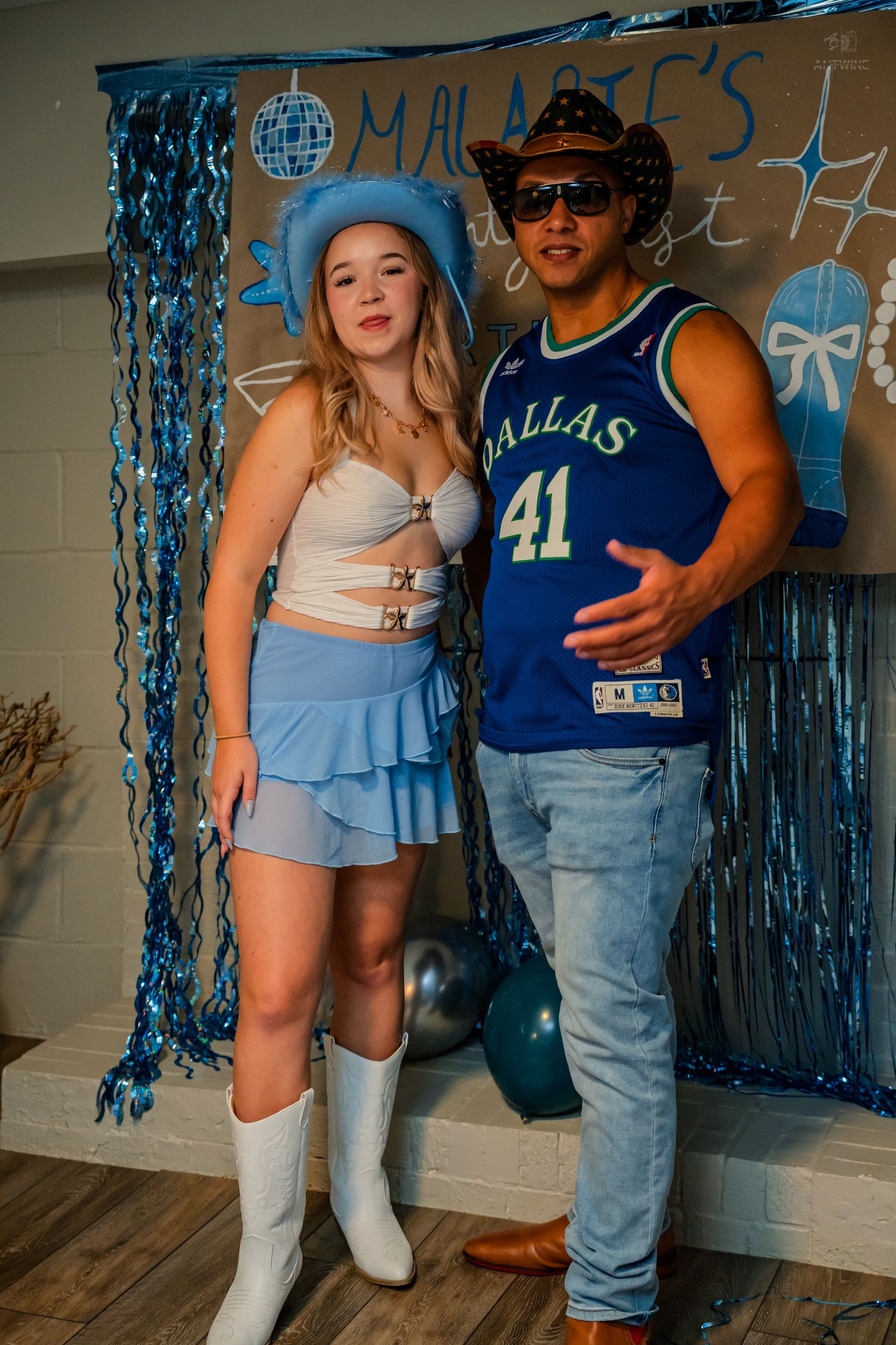 Girl in blue cowboy hat and white boots poses with man in Dallas jersey.