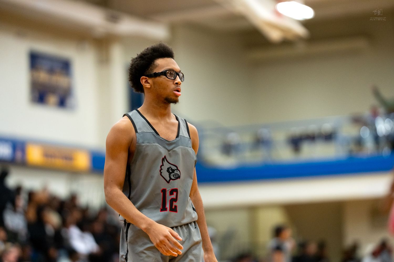 High school basketball player number 12 in gray uniform wearing glasses on the court.