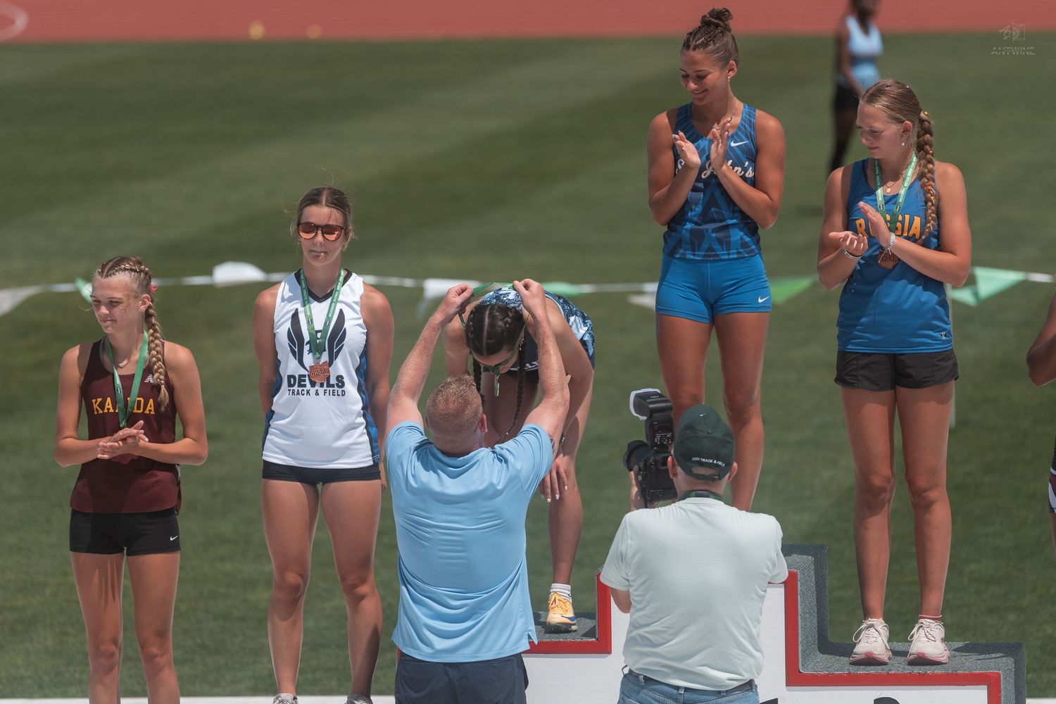 Young female athletes celebrate on podium at OHSAA Division V state track and field championship.