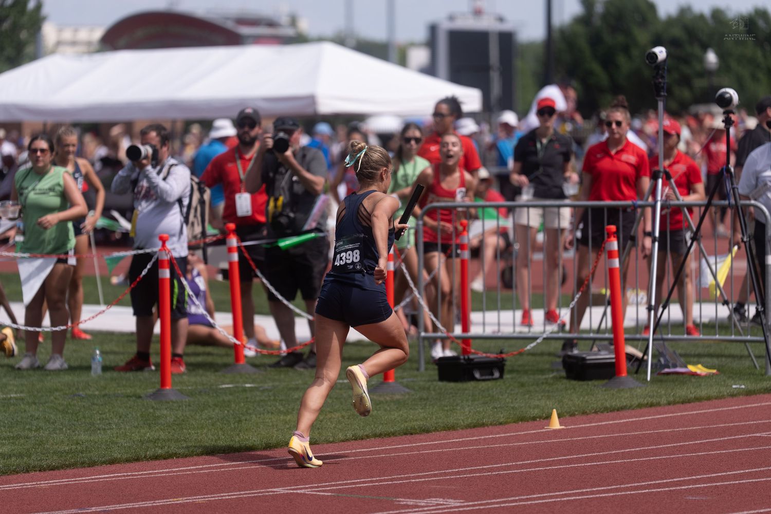 Female track athlete sprints around the curve during a relay race at a high school state championship meet.