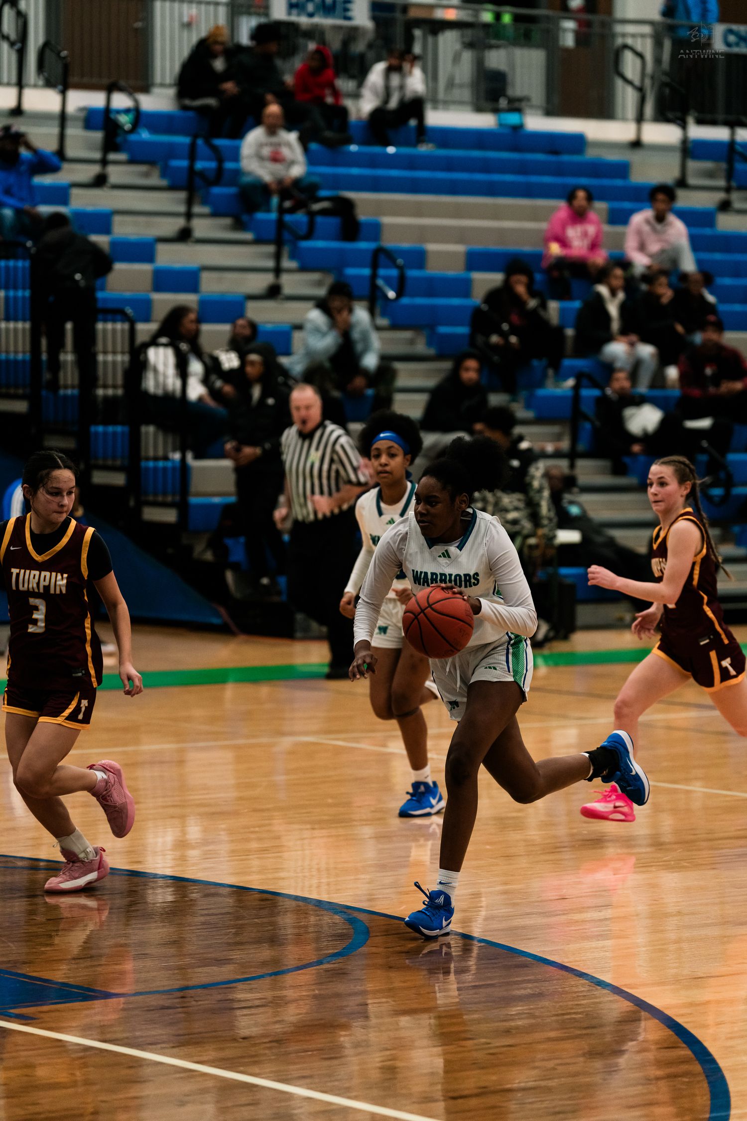 A girls basketball player in teal drives to the basket during a high school game against a maroon team.