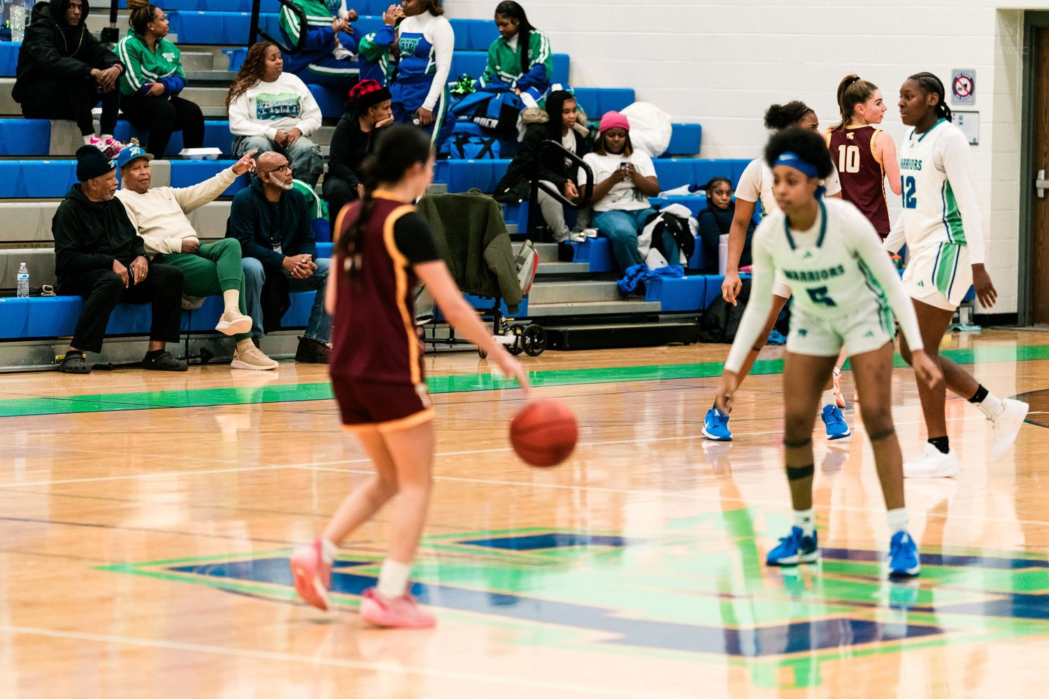 Girls basketball players in teal Warriors uniforms defend against Turpin players during a high school game.