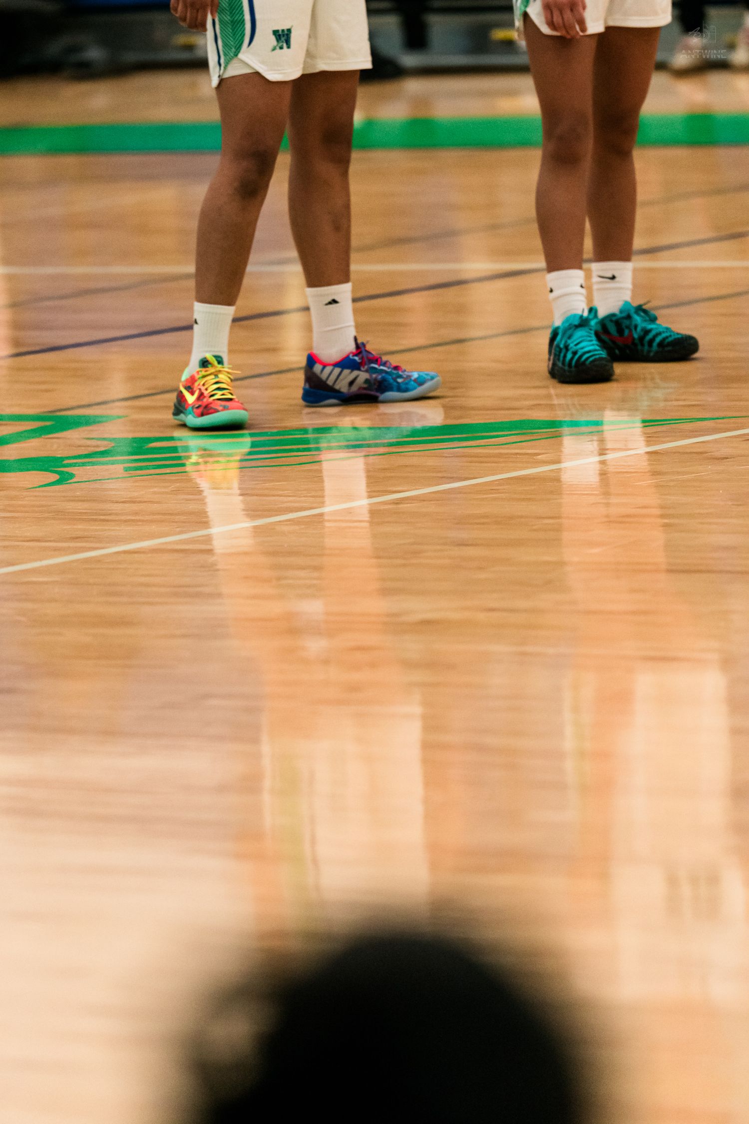 Close-up of colorful basketball sneakers worn by Warriors players standing on a polished hardwood court.