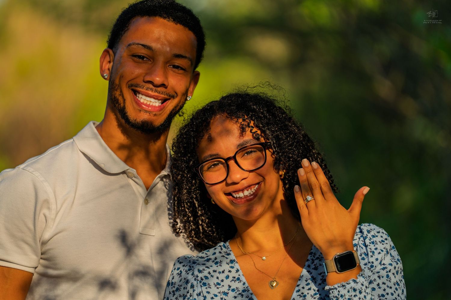 Newly engaged couple smiling outdoors, woman proudly displaying engagement ring on her finger.