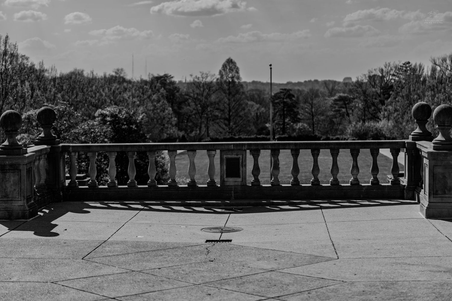 Black and white view from a curved stone balustrade terrace overlooking a wooded landscape and open grounds.