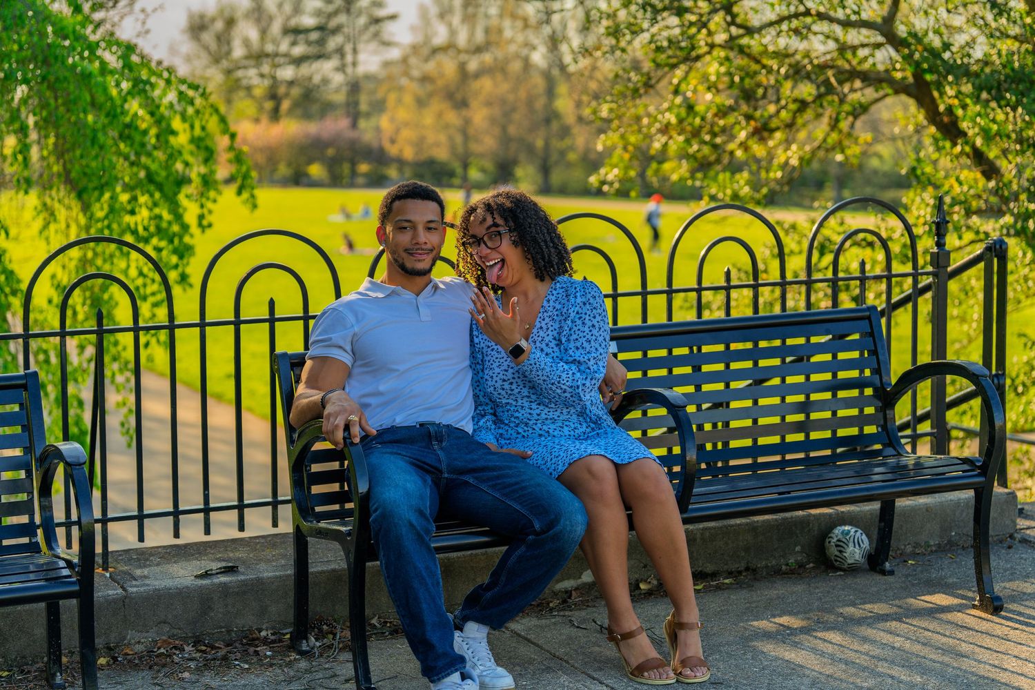 Happy couple smiling and laughing together on a bench in a sunny park setting.