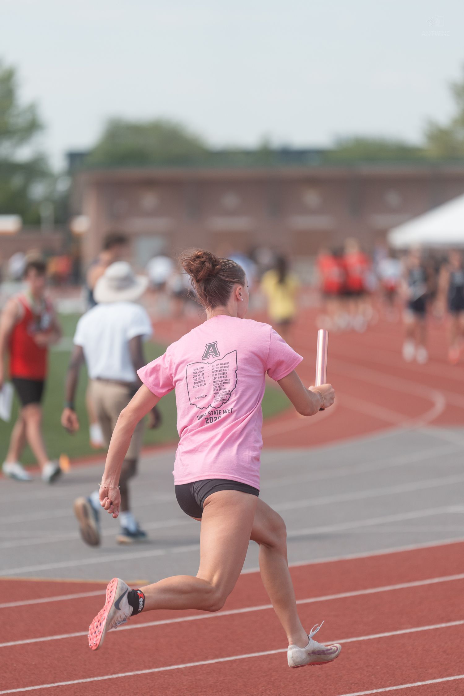 Female athlete in pink shirt runs relay race carrying baton on red track.