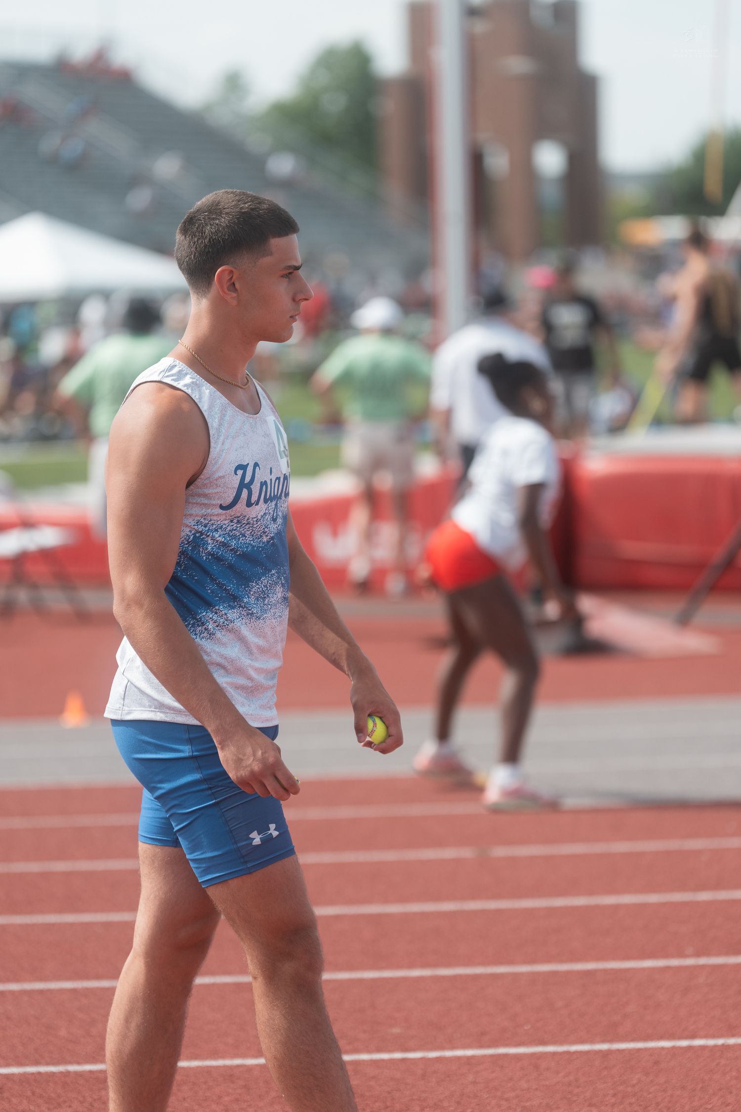Male Knights track athlete holds a baton while standing on red track at outdoor field meet.