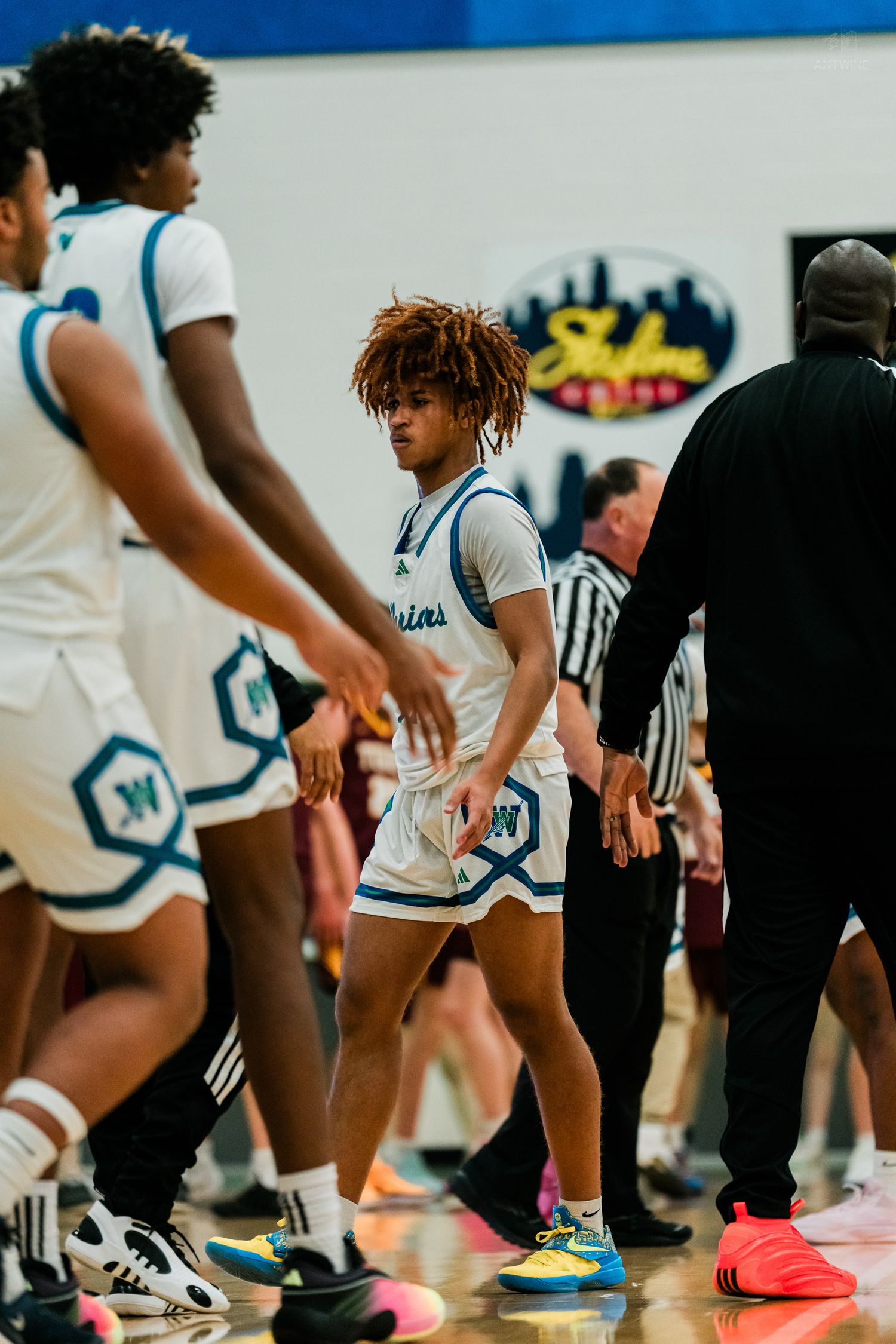 High school basketball player in white Warriors uniform walks through teammate handshake line during pregame warmups.