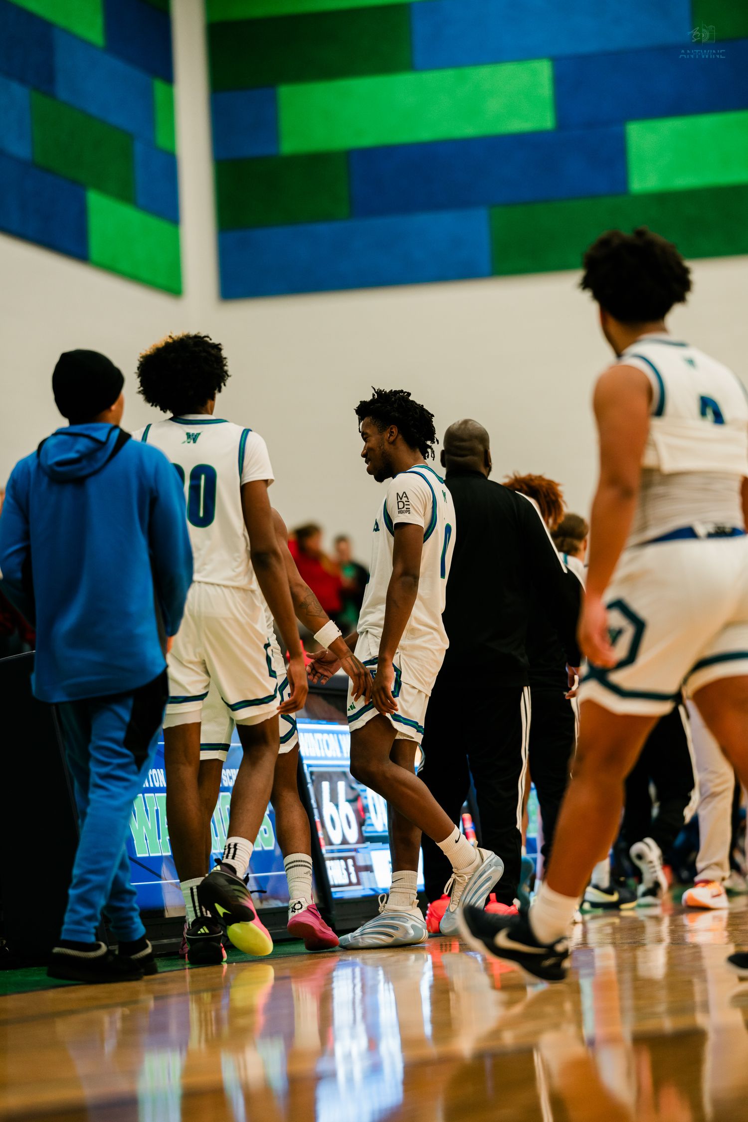 Warriors basketball players huddle near the sideline during a timeout in a high school basketball game.