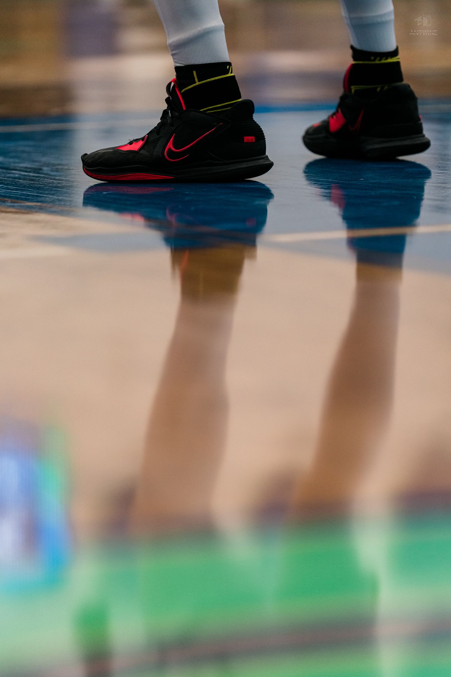 A basketball player wearing black and red Nike high-top sneakers stands on a reflective hardwood court.
