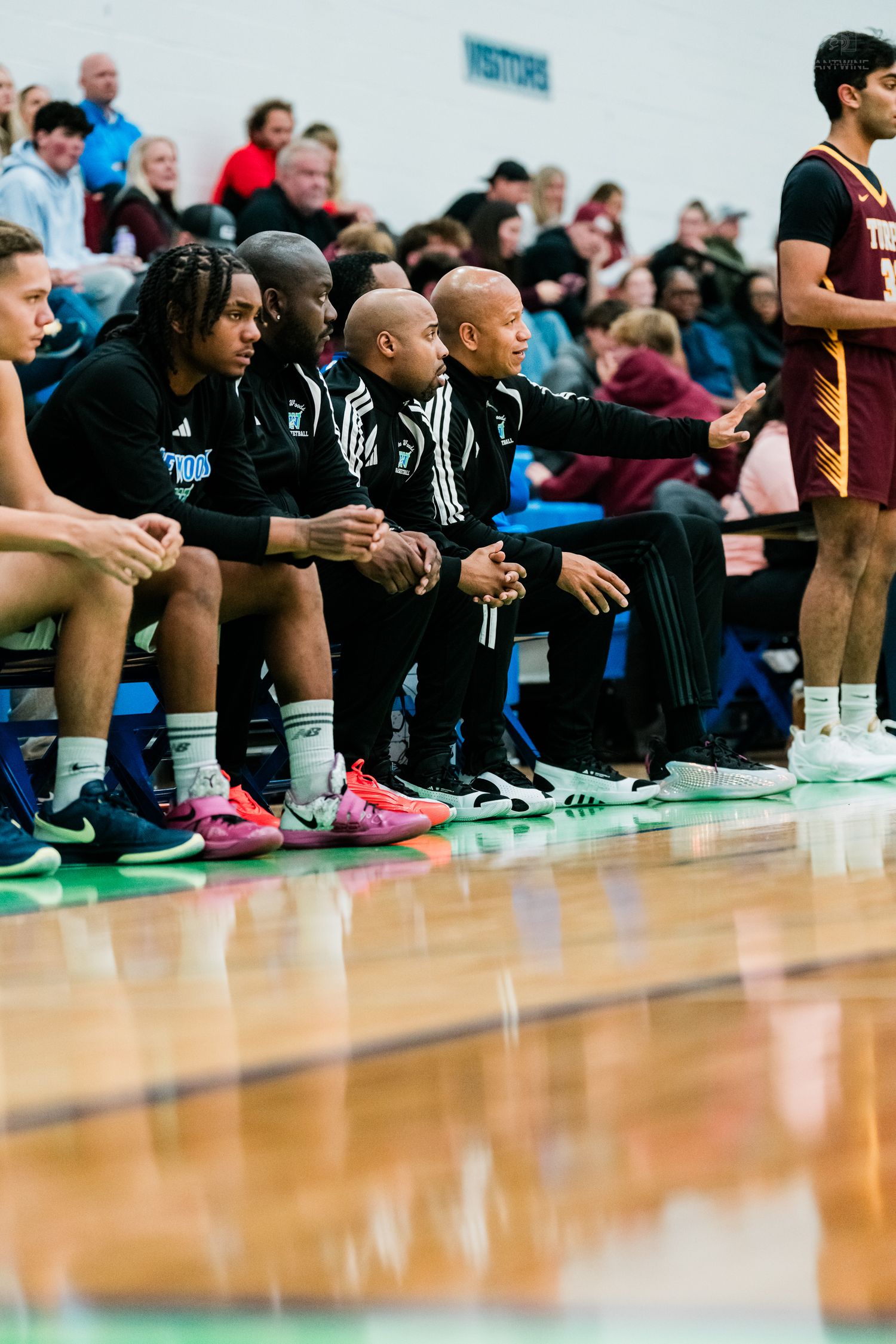 High school basketball coaches and players watch intently from the bench during a game.
