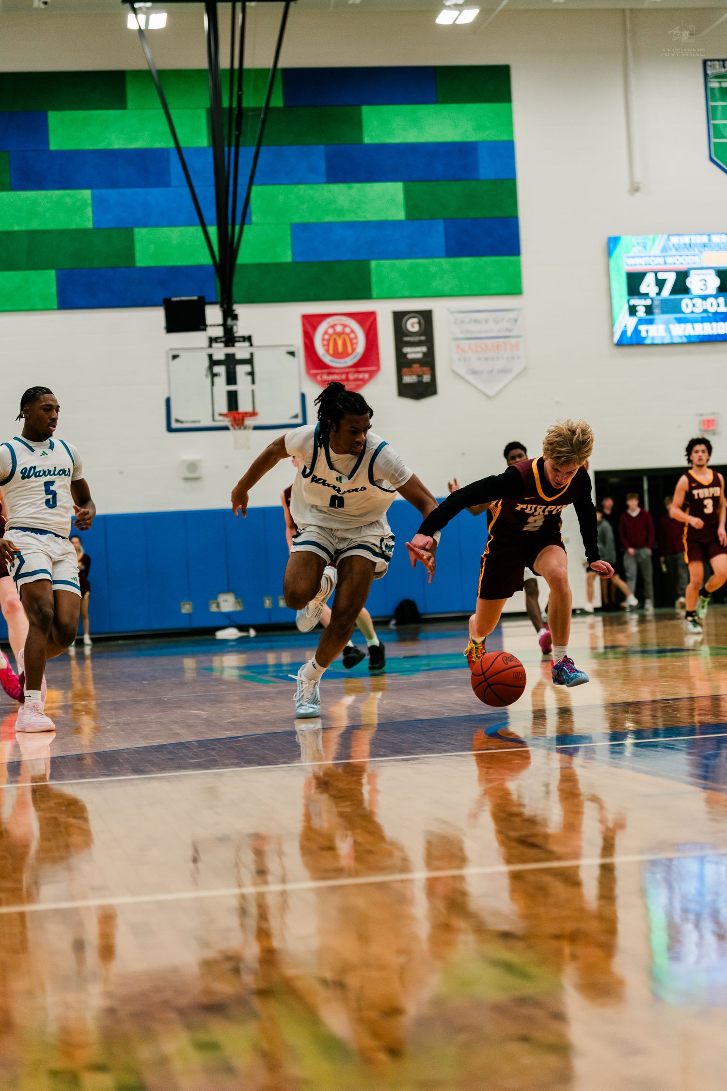 A Warriors defender pressures an opposing player dribbling the ball during a high school basketball game.