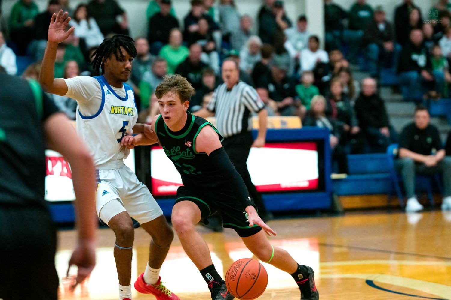 Green-uniformed player drives past defender in competitive high school basketball game.