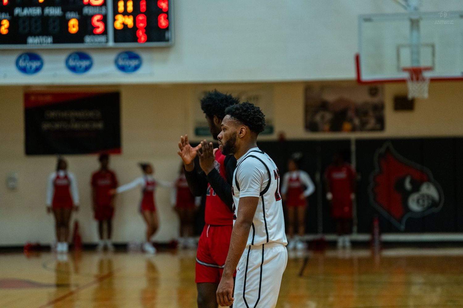 Two high school basketball players stand near the scoreboard during a timeout in a game.