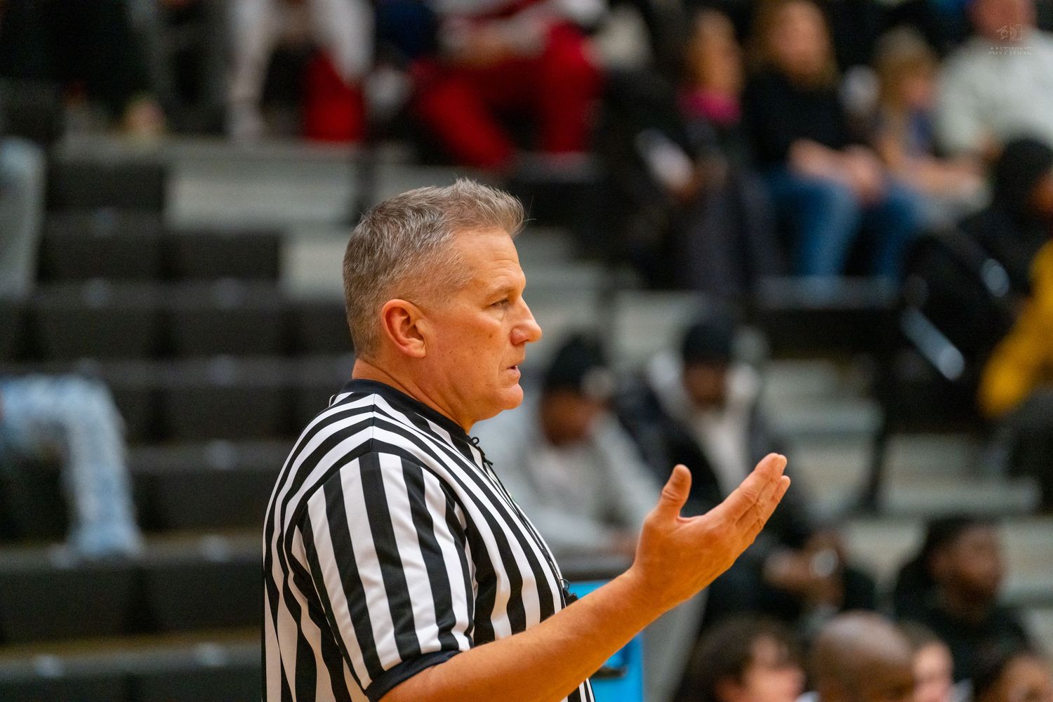 Experienced basketball referee in striped uniform gestures during high school varsity basketball game.