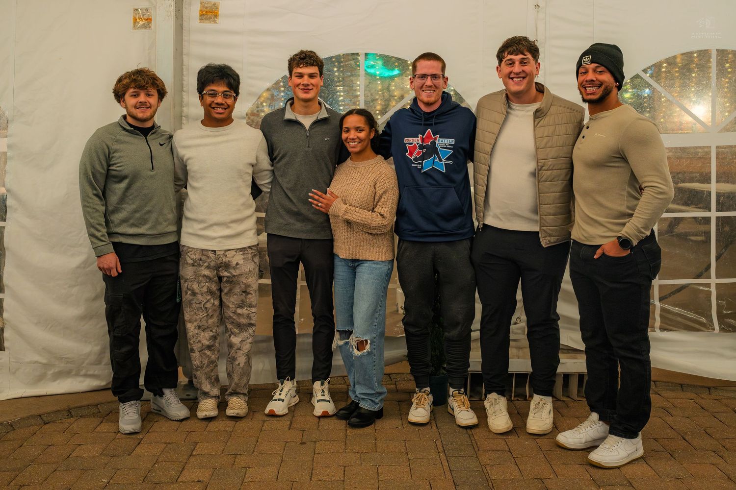 Group of seven friends pose together smiling inside a white event tent.
