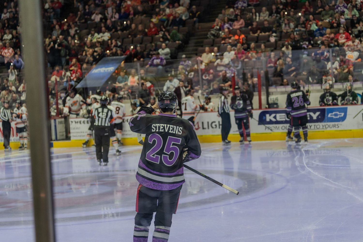 Hockey player Stevens #25 in purple jersey raises stick on ice rink while crowd cheers in background.