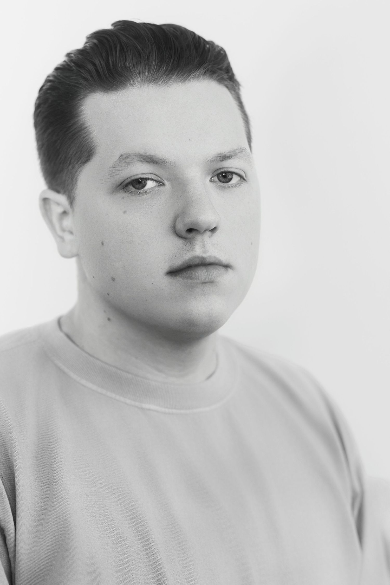 Black and white close-up portrait of young man in sweatshirt with serious expression on white background.