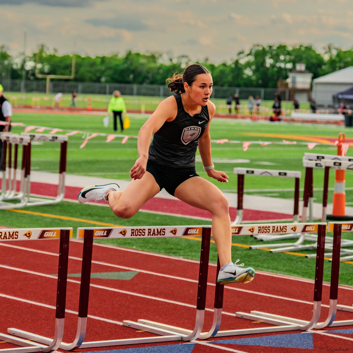 Female athlete in black uniform clears hurdle at Ross Rams track meet.