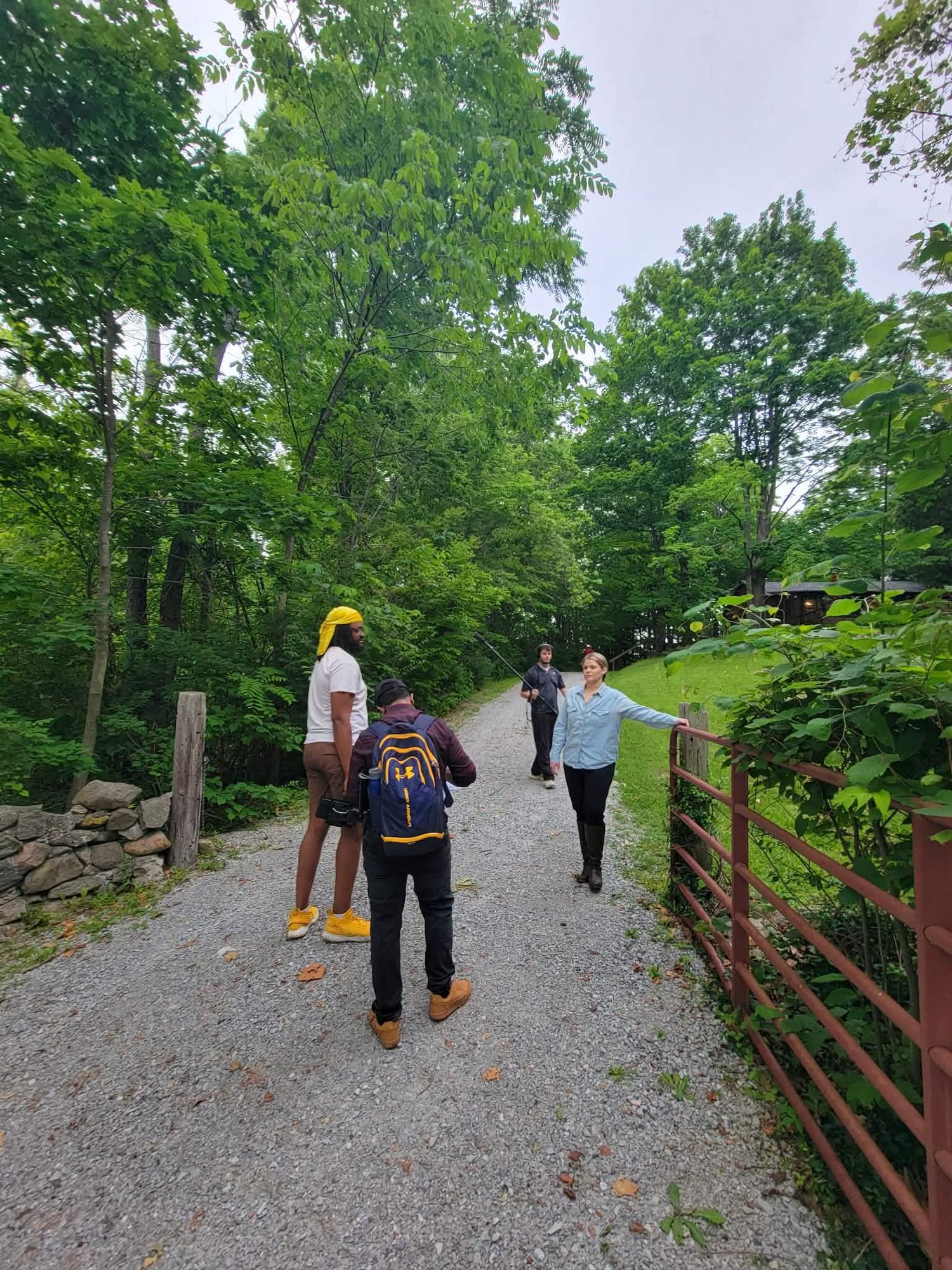 Group of people walking on a gravel trail surrounded by lush green trees and wooden fence.