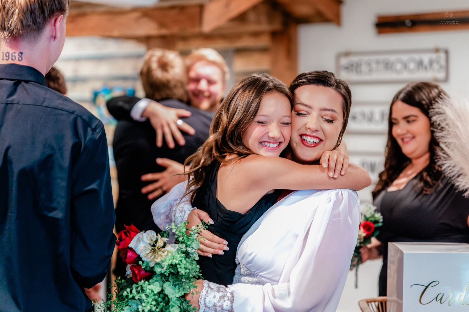 Smiling bride hugs a young girl in black dress warmly at wedding reception venue.