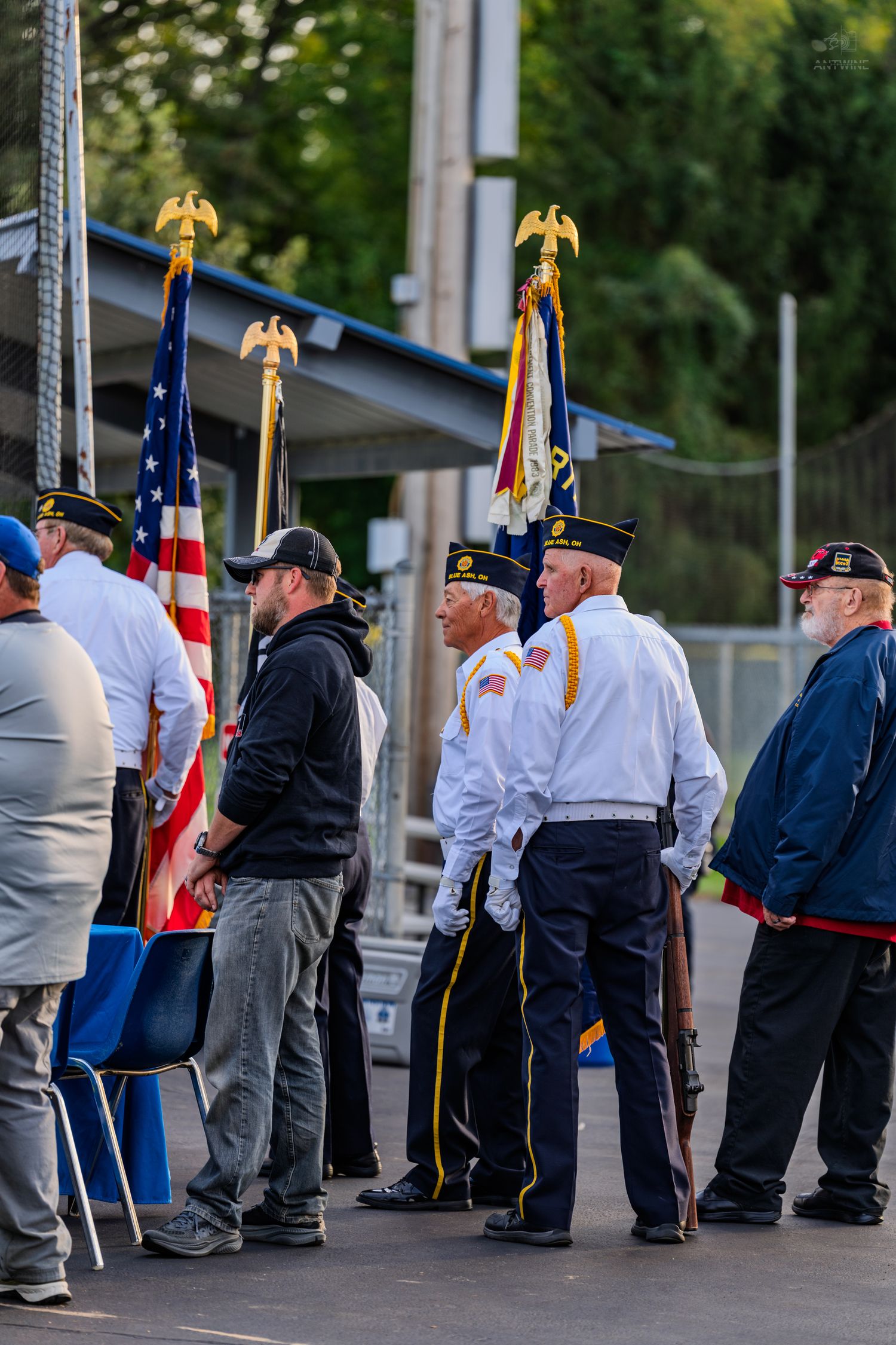 Veterans in uniform stand at attention with American flags during a military color guard ceremony outdoors.