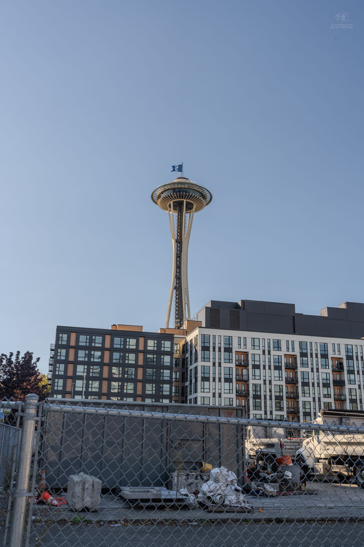 Seattle Space Needle tower rising above residential buildings behind a chain-link construction fence.