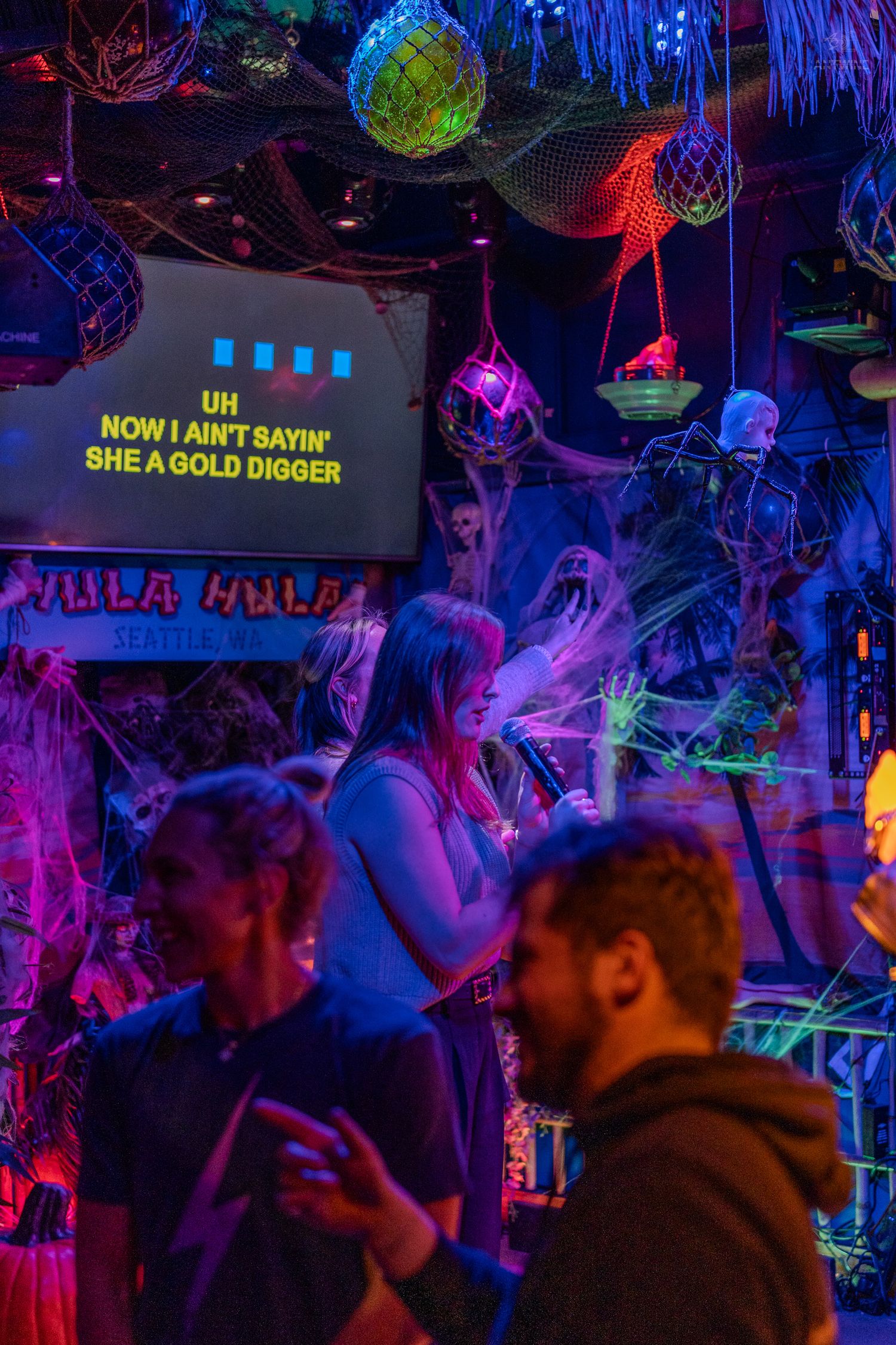 Colorful karaoke bar with neon lights, Halloween decorations, and guests singing Gold Digger at Villa Hula in Seattle.
