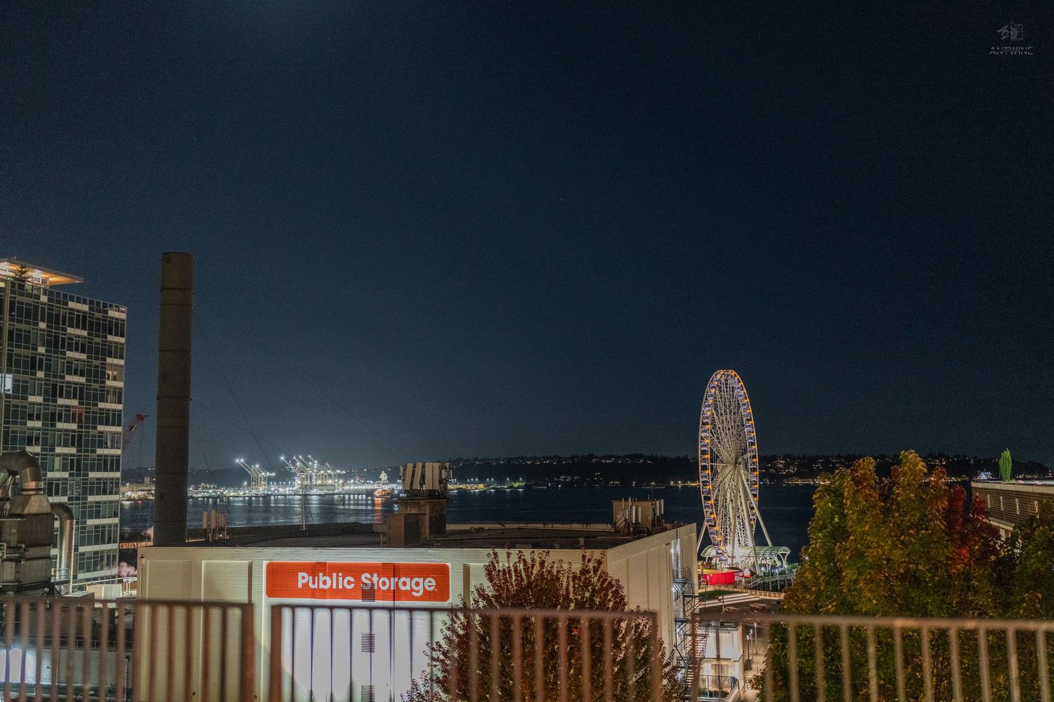 Nighttime Seattle waterfront view with illuminated Great Wheel ferris wheel and Public Storage sign under a dark blue sky.