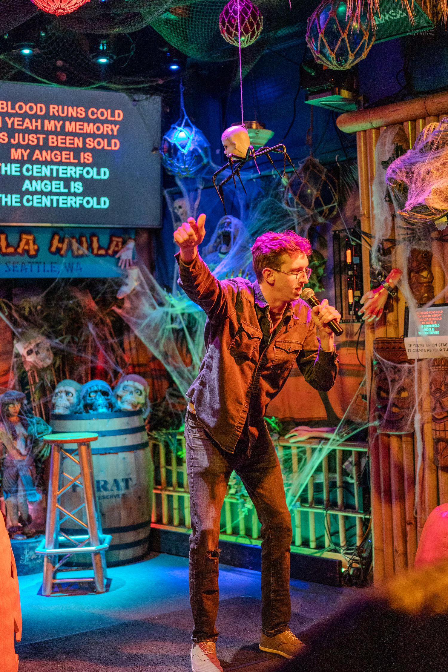 Man singing karaoke on Halloween-decorated stage at Hula Hula bar in Seattle, WA.