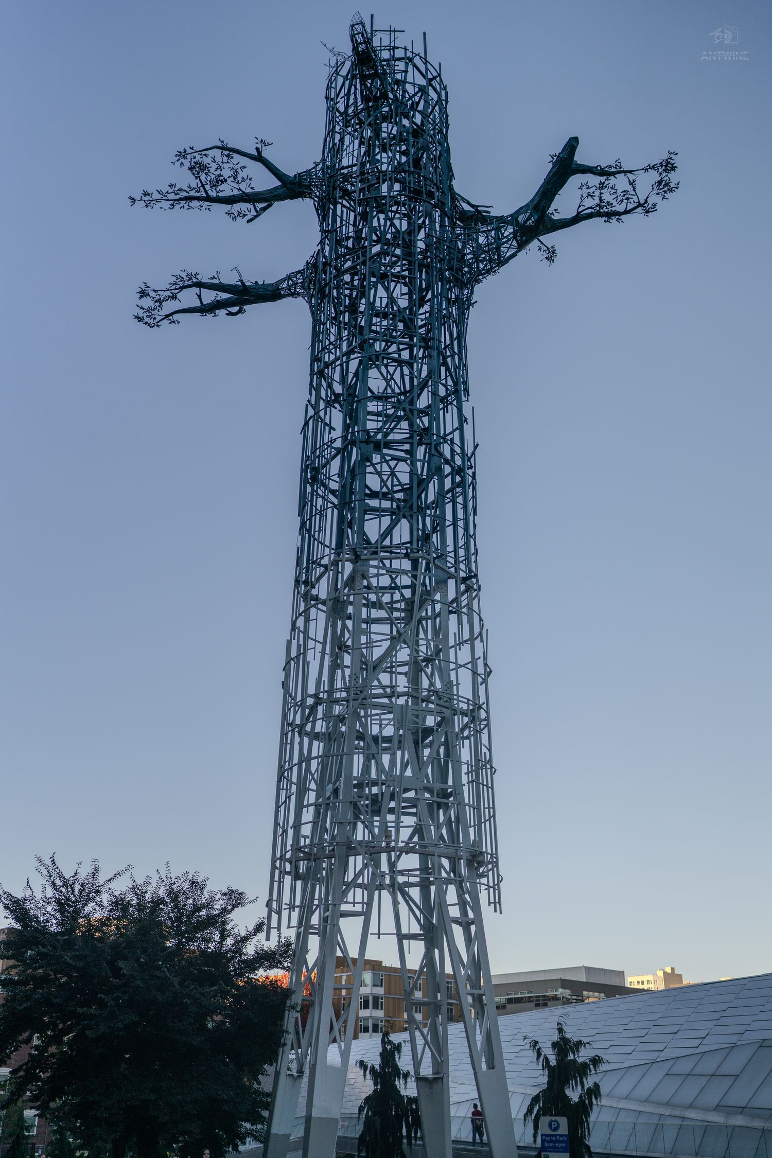 Tall steel lattice sculpture resembling a tree with bare branches silhouetted against a clear dusk sky.